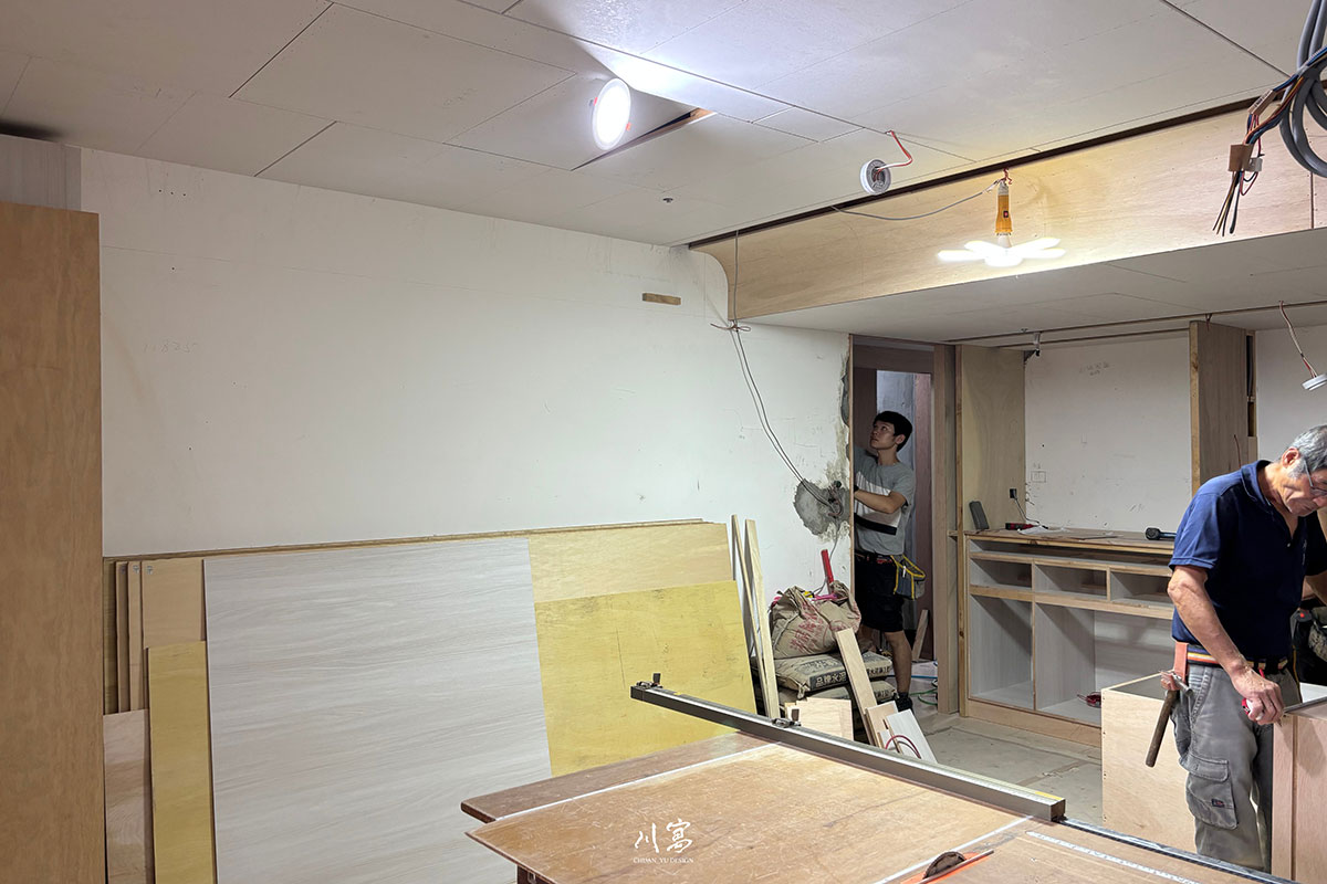 室內裝潢木作工程進度，現場配置板材與鋸台，天花板結構正進行管線隱藏與造型施工。